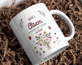 May include: White ceramic mug with a handle, featuring the text "MERCI Citsem DE M'AVOIR AIDÉ À GRANDIR de Maël" in burgundy and black. The mug is decorated with a floral bouquet and butterflies. The mug is presented in a gift box with brown paper.