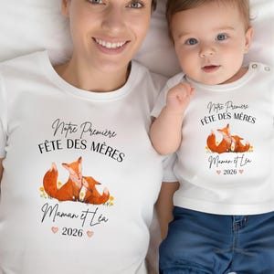 Peut inclure: Deux t-shirts blancs assortis. Ils affichent le texte "Notre Première Fête des Mères" et "Maman et Léa 2026", ainsi qu'une illustration de deux renards. Un t-shirt est pour adulte, l'autre pour bébé.