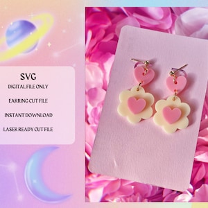 Op de afbeelding: Een paar roze en crèmekleurige hart- en bloembedragende oorbellen. De oorbellen zijn gemaakt van polymer clay en hebben een gouden haak.