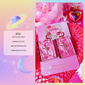 May include: Pink and red earrings with a book-like design, featuring a rose illustration and the words "Love Spells." The earrings are displayed on a pink card with the shop's logo and social media handle. The image also includes a digital file graphic.