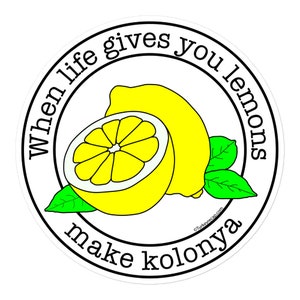 May include: A white circle with a black border and the text "When life gives you lemons make kolonya" in black. Inside the circle are two yellow lemons, one cut in half, with green leaves.