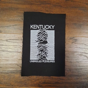 May include: Black rectangular patch with white text and graphic. The word "KENTUCKY" is at the top, above a white, stylized sound wave design. Below the graphic, the words "UNBRIDLED PLEASURES" are printed in white.