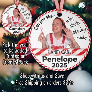 May include: A round Christmas ornament with a red and white candy cane border. The ornament features a woman holding a candy cane, with the text "Can you say..." and "icky sticky sticky sticky". The name "Penelope" and the year "2025" are printed on the ornament.