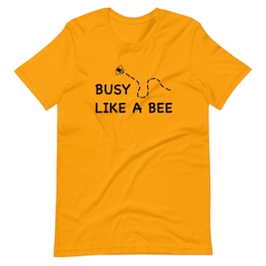 Puede incluir: Una camiseta amarilla de manga corta con un gráfico de abeja negra y el texto "BUSY LIKE A BEE".