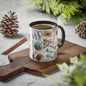 Può includere: Una tazza in ceramica bianca con manico nero. La tazza è decorata con un motivo colorato di illustrazioni a tema Harry Potter, tra cui il castello di Hogwarts, il Boccino d'Oro e le parole "Sempre" e "Muggle".