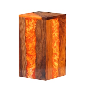 May include: A wooden stool with a rectangular top and a bright orange resin inlay. The resin flows down the side of the stool, creating a unique and modern design.