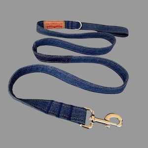 May include: A blue denim dog leash and matching collar. The leash has a silver-colored clasp and a loop handle. The collar features a Levi Strauss & Co. label. The leash and collar are made of blue denim fabric with visible stitching.