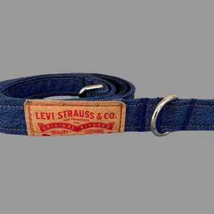 May include: A blue denim dog leash with a metal ring and a rectangular brown label. The label reads "LEVI STRAUSS & CO. SAN FRANCISCO CAL. ORIGINAL RIVETED CLOTHING QUALITY".
