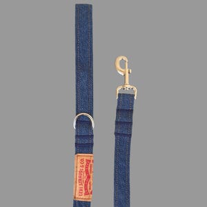 May include: A blue denim dog leash with a silver metal clasp and a D-ring. The leash features a brown leather tag with the "Levi Strauss & Co." logo in red and white.