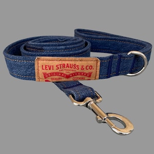 May include: A blue denim dog leash with a silver metal clasp and a matching handle. The leash features a brown rectangular patch with the text "LEVI STRAUSS & CO. ORIGINAL RIVETED CLOTHING".