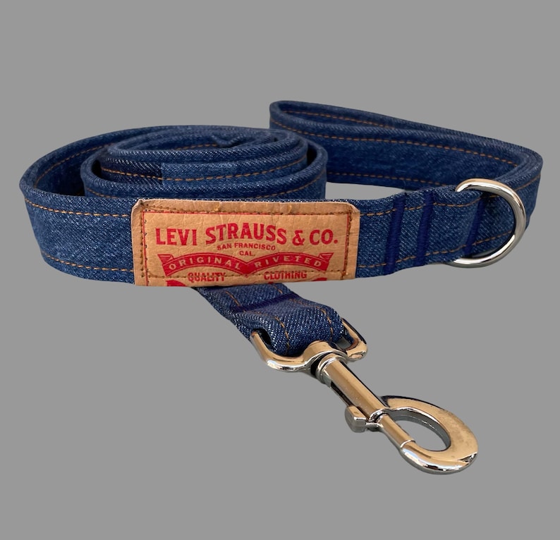 May include: A blue denim dog leash with a silver metal clasp and a matching handle. The leash features a brown rectangular patch with the text "LEVI STRAUSS & CO. ORIGINAL RIVETED CLOTHING".
