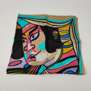 May include: A square scarf featuring a stylized graphic illustration of a face with bold black, pink, turquoise, yellow, and tan colors. The design includes abstract shapes and lines that frame the facial features in a vibrant, multi-colored pattern.