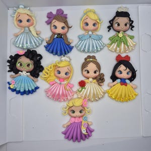 May include: A collection of ten miniature princess dolls with detailed features. Each doll has a unique hairstyle, dress, and accessories, including crowns, bows, and flowers. The dresses are in various colors, such as blue, pink, yellow, and green.