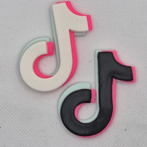 May include: Two musical note-shaped charms. One is white with a pink outline and a light blue inner layer. The other is black with a pink outline and a light blue inner layer. The charms are on a white background.