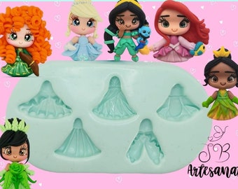 Puede incluir: Una colección de figuras de princesas hechas a mano, cada una con características y atuendos únicos, junto con un molde de silicona azul claro con diseños de vestidos. Las figuras incluyen personajes con cabello rojo, rubio y negro, vistiendo vestidos de varios colores.