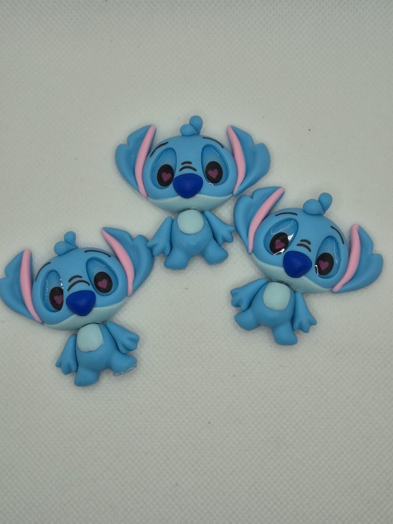 Puede incluir: Tres figuras azules de un personaje con orejas grandes, interior de las orejas rosa y ojos en forma de coraz&oacute;n. Las figuras tienen una nariz azul y un cuerpo peque&ntilde;o y redondo. Est&aacute;n dispuestas sobre una superficie blanca.