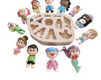 Puede incluir: Una colección de coloridas figuras en miniatura, incluyendo una sirena, un pirata y otros personajes, rodea un molde de silicona beige. Las figuras están en varias poses y atuendos, con detalles como sombreros, vestidos y expresiones faciales. El molde tiene varias cavidades.