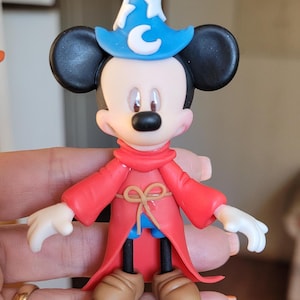 Könnte beinhalten: Eine rote und blaue Figur von Mickey Mouse, der als Zauberer verkleidet ist. Er trägt einen blauen Hut mit einem weißen Stern und einem Halbmond, eine rote Robe mit einem braunen Gürtel und braune Schuhe.