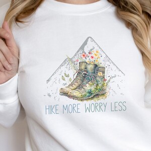 May include: White sweatshirt with a graphic of hiking boots and a mountain with the text "Hike More Worry Less".