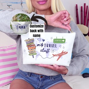 May include: White travel pouch with a gold zipper, featuring the text "my TRAVEL stuff" and a world map design. Includes a red airplane graphic, directional signs to various cities, and the option to customize the back with a name.