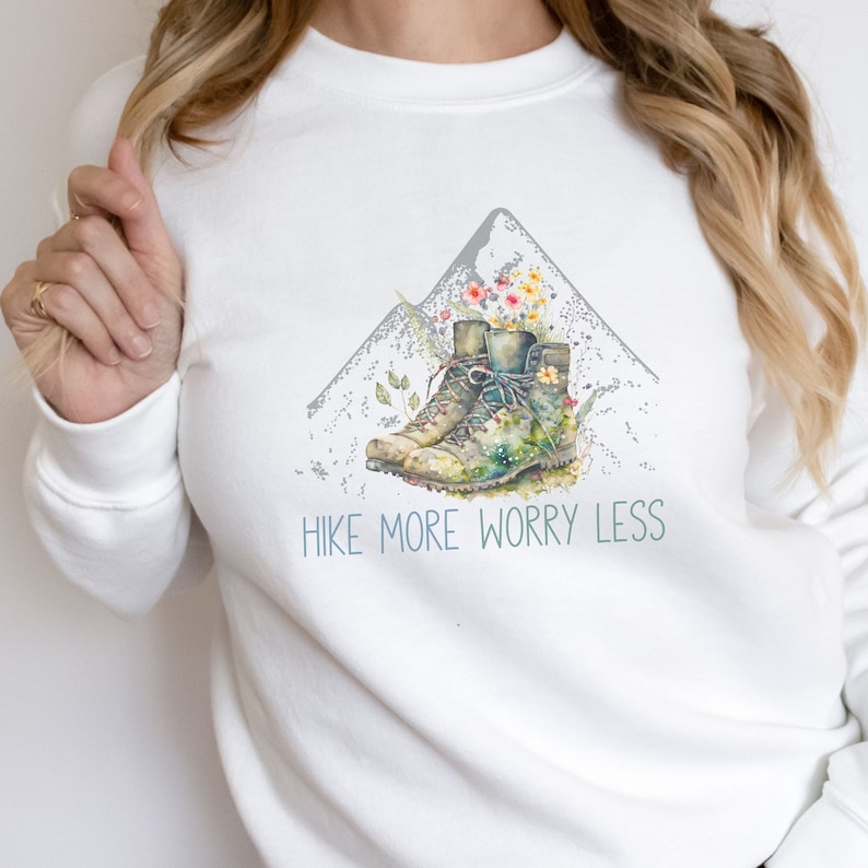 May include: White sweatshirt with a graphic of hiking boots and a mountain with the text "Hike More Worry Less".