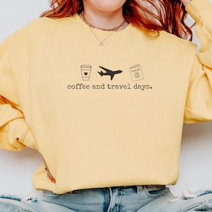 Puede incluir: Sudadera amarilla con un gr&aacute;fico negro de una taza de caf&eacute;, un avi&oacute;n y un pasaporte. El texto "coffee and travel days." est&aacute; impreso debajo. La sudadera es de estilo casual.