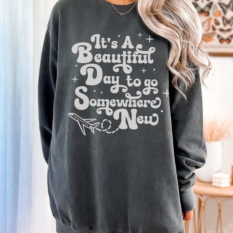 以下が含まれることがあります： 「It's A Beautiful Day to go Somewhere New」の白文字と飛行機のグラフィックが特徴のダークグレーのスウェットシャツ。クルーネックのスウェットシャツはカジュアルなスタイルです。