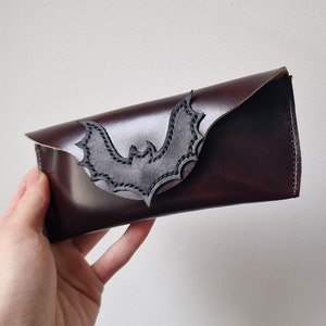 May include: A burgundy leather glasses case with a black bat cutout design.