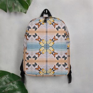 以下が含まれることがあります： 蝶と波のカラフルな模様が施された黒いバックパック。模様は左右対称で、青、オレンジ、黄色、白など様々な色が使われています。