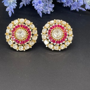 Può includere: Un paio di orecchini rotondi in oro con un design circolare di pietre preziose bianche e rosa. Gli orecchini hanno una pietra preziosa bianca rotonda centrale circondata da pietre preziose bianche più piccole e un anello di pietre preziose rosa.