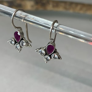 Può includere: Un paio di orecchini pendenti in argento con una pietra preziosa viola e pietre di zircone cubico trasparenti.