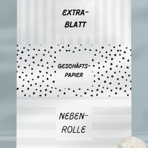 May include: A white and gray striped background with three text blocks: "EXTRA-BLATT", "GESCH&Auml;FTS-PAPIER", and "NEBEN-ROLLE". The middle section has a black polka dot pattern. A seashell and small white stones are in the foreground.