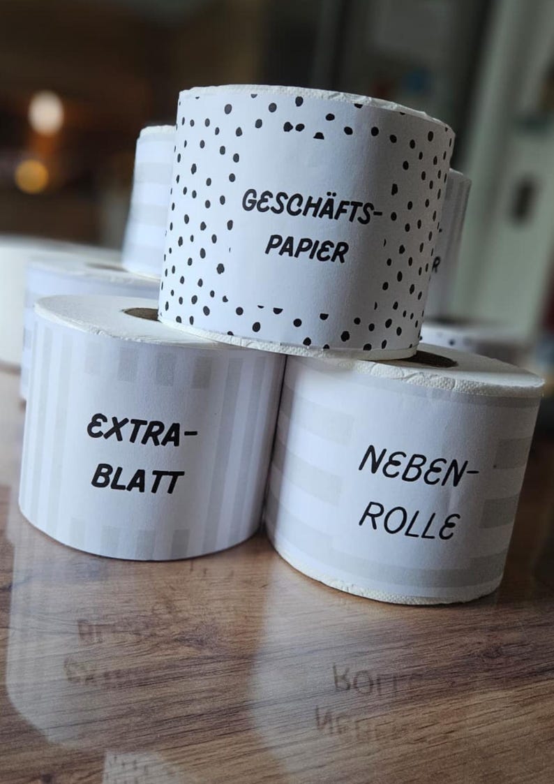 May include: Close-up of several rolls of white paper with text labels. One roll has a black polka dot pattern, while others have vertical stripes. The labels include the words "EXTRA-BLATT" and "NEBEN-ROLLE".