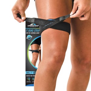May include: Black IT Band Strap for the iliotibial band. The strap is being adjusted on a person's thigh. The product packaging is visible, with the text "CROSSTRAP BY MOUS" and "IT BAND STRAP FOR THE ILIOTIBIAL BAND". The size is listed as "SMALL: 17"-23"".
