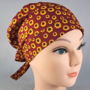 May include: A maroon scrub hat with a sunflower pattern. The hat has a tie at the back.