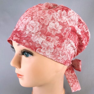 May include: A pink and white floral print scrub hat with a tie at the back.