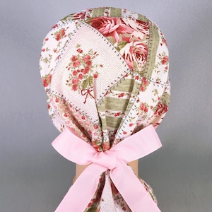 Puede incluir: Un gorro de quirófano de color rosa y blanco con un lazo rosa atado en la parte posterior. El gorro tiene un diseño de patchwork con motivos florales y rayas verdes.