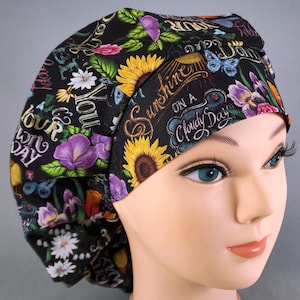 May include: Black scrub hat with a floral and sunflower print. The hat has the text "You are the sunshine on a cloudy day" printed on it.