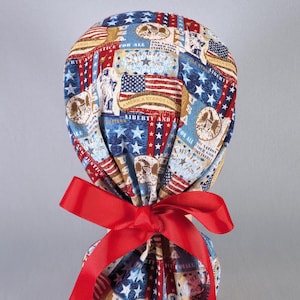 May include: A patriotic scrub cap featuring a red bow. The cap is patterned with American flags, stars, and patriotic text. The design incorporates red, white, and blue colors, creating a festive and thematic appearance.