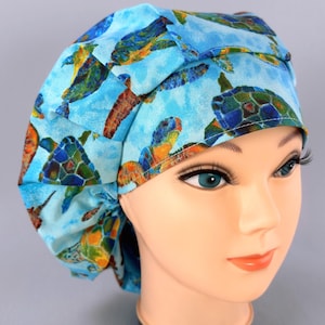 May include: A blue surgical scrub cap featuring a pattern of sea turtles in shades of blue, green, and orange. The cap is made of fabric and is designed to cover the head. The cap is shown on a mannequin head.