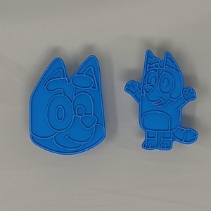 May include: Two blue plastic cookie cutters shaped like a cartoon dog. One cutter shows the dog's face and the other shows the dog's full body.