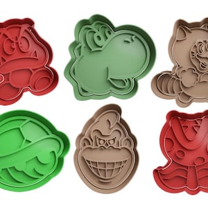 May include: Six different cookie cutters shaped like characters from the Super Mario Bros. video game series. The cutters are made of red, green, brown, and beige plastic. The characters include Bowser, Yoshi, Toad, Donkey Kong, Goomba, and a Raccoon Mario.
