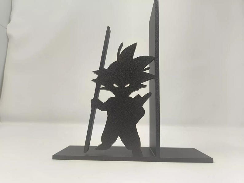 May include: Black silhouette of a character from Dragon Ball Z, holding a staff, used as a bookend. The bookend is made of a solid material and has a rectangular base. The character is in a dynamic pose.