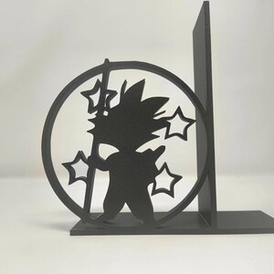 May include: Black silhouette of a character holding a staff, surrounded by a circle and stars, used as a bookend. The bookend is made of a solid material and has a base for stability. The design is a stylized representation of a popular anime character.