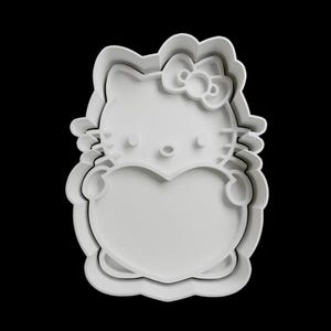 May include: White plastic cookie cutter shaped like a cartoon cat holding a heart. The cat has a bow on its head and a heart-shaped body.