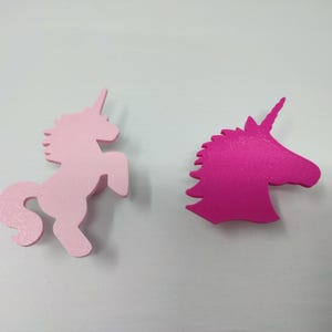 May include: Two unicorn shapes, one pink and one hot pink. The pink unicorn is standing on all four legs, while the hot pink unicorn is only a head and neck.