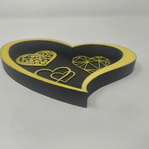 May include: A heart-shaped decorative tray with a black interior and a yellow border. The tray features three heart designs: a filigree heart, a geometric heart, and two interlocking hearts.