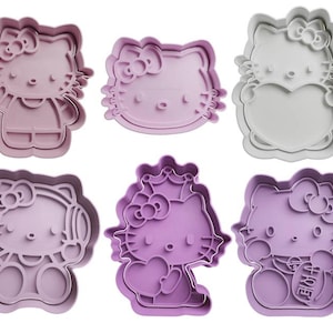May include: Set of six purple plastic cookie cutters shaped like Hello Kitty characters. The cutters feature different poses and expressions, including Hello Kitty holding a heart, wearing a crown, and holding a microphone.