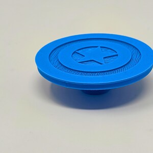 May include: A blue plastic 3D printed model of Captain America's shield. The shield has a white star in the center and a textured surface.