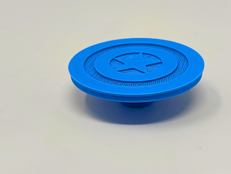 May include: A blue plastic 3D printed model of Captain America's shield. The shield has a white star in the center and a textured surface.